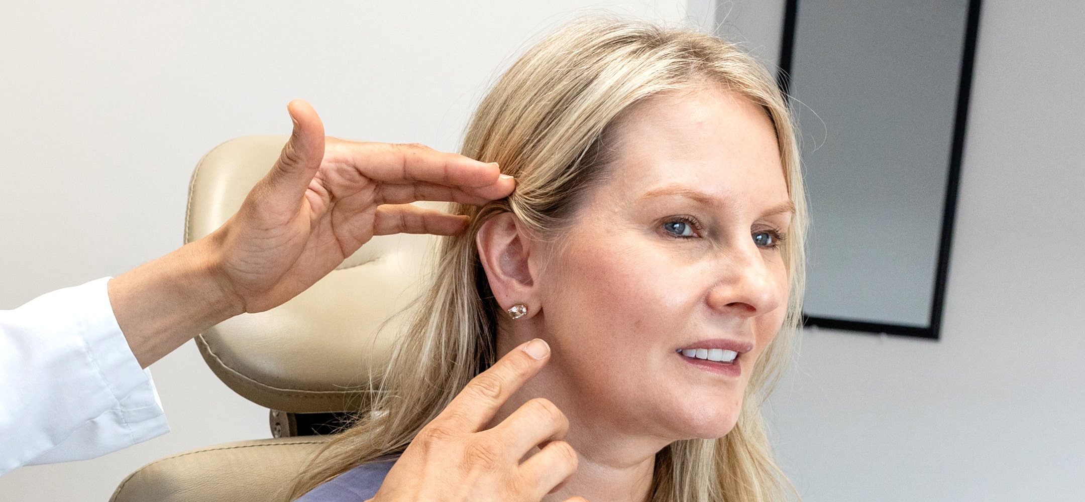 A person undergoes an ear examination by another person in a clinical setting, focusing on ear aesthetics and potential enhancements.